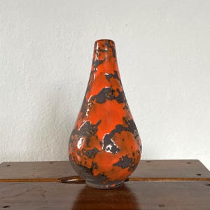 Könnte beinhalten: Eine kleine, orangefarbene und schwarze Keramikvase in Tropfenform. Die Vase hat eine gefleckte Glasur mit einer strukturierten Oberfläche.