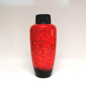 May include: A cylindrical vase featuring a glossy black neck and base, with a vibrant red body displaying a mottled, cloud-like texture. The surface transitions from the solid black base to the bright red midsection and back to a solid black rim.