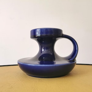 Könnte beinhalten: Eine glänzende, dunkelblaue Keramikvase mit einem einzigartigen, skulpturalen Design. Die Vase hat einen breiten, abgerundeten Boden, einen ausgestellten Mittelteil und eine zylindrische Oberseite mit einem Griff. Die Gesamtform ist organisch und modern, geeignet für die Inneneinrichtung.