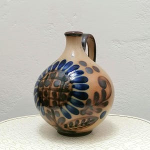 May include: A brown ceramic jug with a blue and brown floral design. The jug has a handle and a round body.