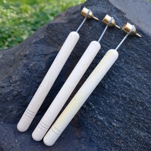 May include: Three wooden handled tools with brass tips. The tips are different sizes and shapes. The tools are laid out on a dark gray rock surface.