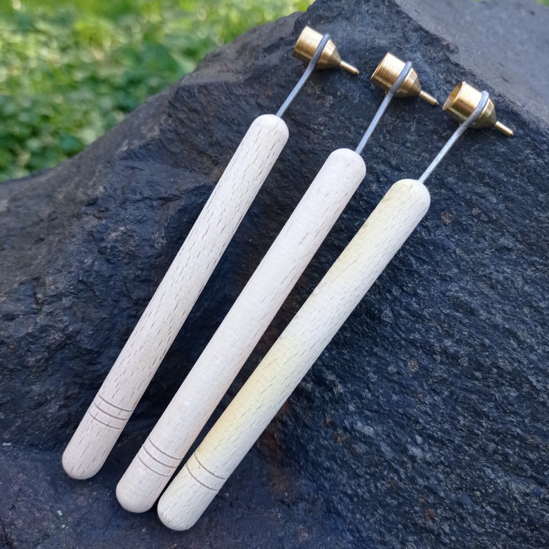 May include: Three wooden handled tools with brass tips. The tips are different sizes and shapes. The tools are laid out on a dark gray rock surface.