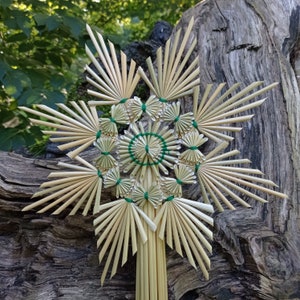 Könnte beinhalten: Ein sternförmiges Ornament aus hellbeigem Naturstroh mit komplexen geometrischen Mustern und strahlenden Spitzen. Die Struktur wird durch einen dünnen grünen Faden zusammengehalten, was ein symmetrisches Design mit einem zentralen Motiv ergibt.