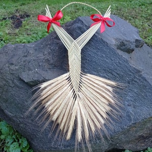 May include: A decorative wall hanging crafted from woven straw and dried wheat stalks. The piece features a central braided straw structure, two bright red satin ribbon bows at the top, and a wide, fan-shaped base made of natural golden wheat heads.