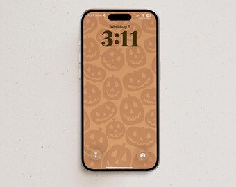 May include: A smartphone displaying a lock screen with a tan background featuring a repeating pattern of dark tan jack-o'-lanterns. The screen shows the date Wed Aug 5 and the time 3:11 in a dark brown font, along with flashlight and camera icons.