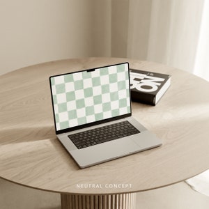 Op de afbeelding: Een zilveren laptop met een groen-wit geruit patroon op het scherm. De laptop is open en staat op een lichtbruine houten tafel. De tekst "NEUTRAL CONCEPT" is op de tafel gedrukt.