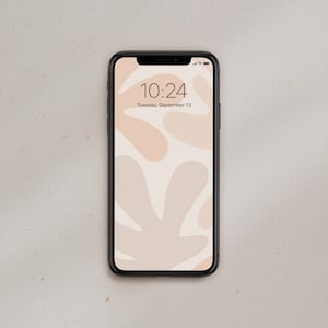 K&ouml;nnte beinhalten: Ein schwarzes Smartphone mit wei&szlig;em Hintergrund und einem abstrakten Muster aus beigefarbenen und hellbraunen Formen. Die Uhrzeit ist 10:24 Uhr und das Datum ist Dienstag, 13. September.