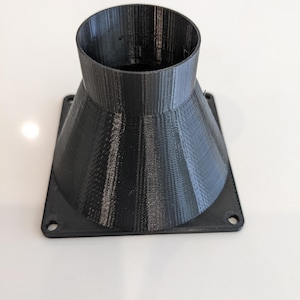 May include: A black 3D printed plastic adapter with a square base and a round opening. The adapter has a conical shape.