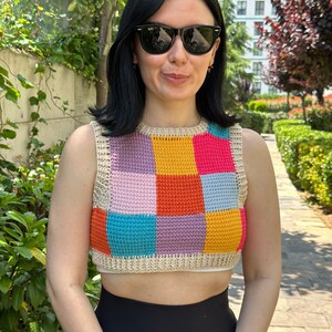 May include: A colorful crochet top with a patchwork design in shades of pink, yellow, orange, blue, and turquoise. The top is sleeveless and has a cropped length.