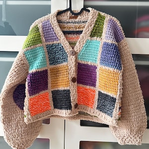 Può includere: Un cardigan in crochet beige con un design a patchwork che presenta quadrati di vari colori, tra cui turchese, viola, arancione e giallo. Il cardigan ha un collo a V e una chiusura con bottone.