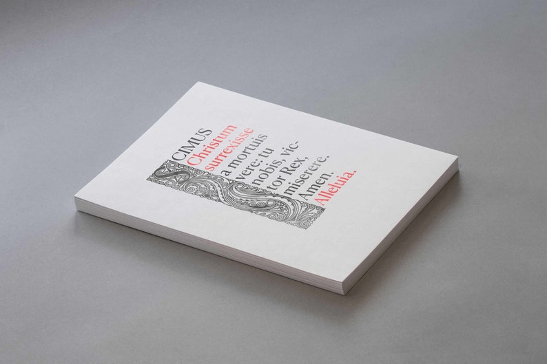 May include: A white book with black and gray text and a decorative design on the cover. The text reads "CIMUS Christum surrexisse a mortuis vere: tu nobis, vic-tor Rex, miserere. Amen. Alleluia."