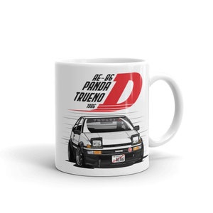 May include: White ceramic mug featuring a graphic of a white and black car with the text "AE-86 Panda Trueno 1986" and a large red "D" on the side. The mug has a white handle and is set against a white background.