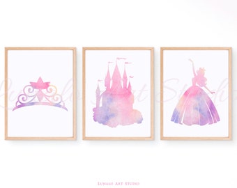 May include: Three watercolor prints featuring a pink and purple castle, a princess silhouette, and a tiara. The prints are framed in a light wood frame.