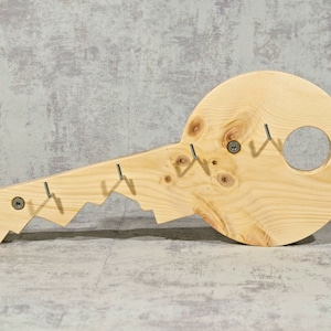 Può includere: Un gancio da parete in legno a forma di chiave con più ganci per appendere oggetti. Il gancio è in legno marrone chiaro e presenta una venatura del legno naturale.