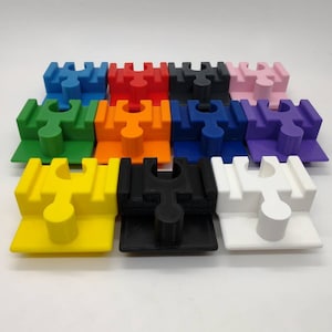 Könnte beinhalten: Zwölf Puzzleteile in verschiedenen Farben, darunter Rot, Blau, Grün, Gelb, Orange, Lila, Pink, Schwarz und Weiß. Jedes Teil hat eine einzigartige Form und ein kleines Loch in der Mitte.