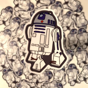 May include: A white and gray R2-D2 robot sticker with blue details. The sticker is on a background of many other R2-D2 stickers.