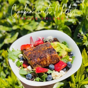 May include: A white bowl filled with a salad featuring grilled salmon, strawberries, blueberries, avocado, and almonds. The bowl is held by a hand against a green leafy background. The text "Cookin' with Chels! EBOOK VOLUME 2" is at the top of the image. The text "Get ready to transform some of your favorite dishes into pescatarian and vegan options. With over 20 recipes to choose from, you will be eating clean in no time." is at the bottom of the image. The text "CHELSEA RENEE' Co-Owner of GetRightWithPnC" is at the bottom of the image.