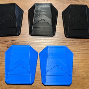 May include: Five plastic shapes, three black and two blue, with a geometric design. The shapes are all the same size and have a slightly rounded, rectangular shape.