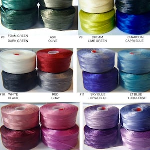 May include: A collection of 13 spools of embroidery floss in various colors, including green, blue, red, white, and purple. Each spool is labeled with a number and a color name.