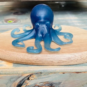 May include: A blue octopus figurine with a smooth, glossy finish. The octopus is sitting on a wooden surface.