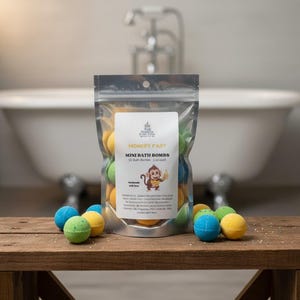 May include: A clear bag of "Monkey Fart" mini bath bombs, with a cartoon monkey graphic. The bag contains 10 bath bombs, each 1 oz. Several colorful bath bombs are scattered on a wooden surface in front of a white bathtub.