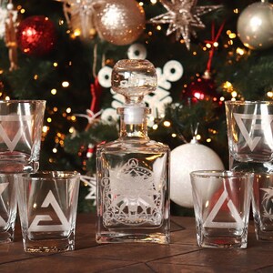 K&ouml;nnte beinhalten: Ein Set aus sechs klaren Gl&auml;sern mit ge&auml;tzten geometrischen Mustern, darunter eine Karaffe mit einem &auml;hnlichen Muster. Die Gl&auml;ser und die Karaffe sind auf einer Holzoberfl&auml;che vor einem Weihnachtsbaum mit Ornamenten angeordnet.