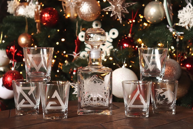 K&ouml;nnte beinhalten: Ein Set aus sechs klaren Gl&auml;sern mit ge&auml;tzten geometrischen Mustern, darunter eine Karaffe mit einem &auml;hnlichen Muster. Die Gl&auml;ser und die Karaffe sind auf einer Holzoberfl&auml;che vor einem Weihnachtsbaum mit Ornamenten angeordnet.