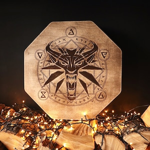 K&ouml;nnte beinhalten: Ein achteckiges Schild aus Holz mit einem Wolfskopf und einem geometrischen Design. Das Schild ist von einer Lichterkette umgeben.