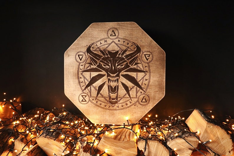 K&ouml;nnte beinhalten: Ein achteckiges Schild aus Holz mit einem Wolfskopf und einem geometrischen Design. Das Schild ist von einer Lichterkette umgeben.