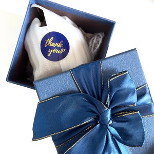 May include: A blue gift box with a gold ribbon and a blue circle sticker that says "thank you" with a gold heart.
