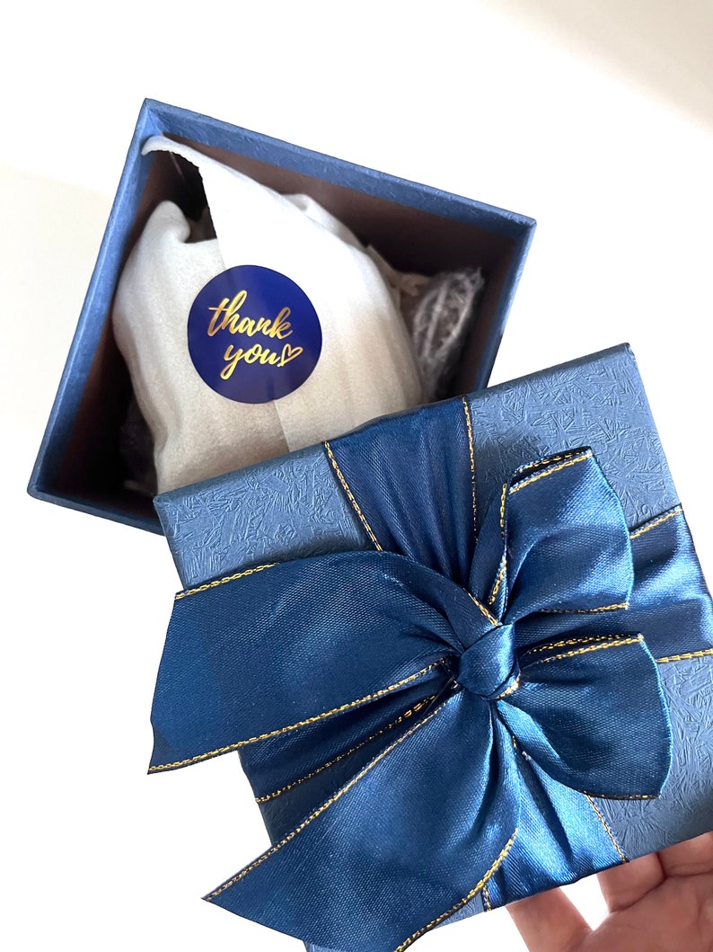 May include: A blue gift box with a gold ribbon and a blue circle sticker that says "thank you" with a gold heart.