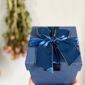 May include: A navy blue gift box with a gold ribbon and bow.