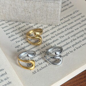 May include: Three open-style rings with a smooth, curved design. One ring is gold-toned, one is silver-toned, and one is a two-toned combination featuring a gold-coloured band with a silver-coloured accent piece. The rings have a polished finish.