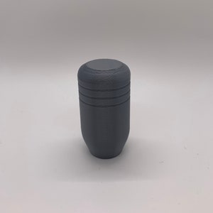 Puede incluir: Una palanca de cambios cilíndrica gris con una superficie texturizada.