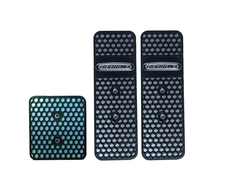 May include: Three black metal pedal pads with a honeycomb pattern and the word "FREIGHTLINER" in silver lettering.