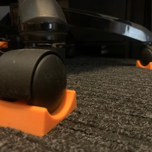 May include: Close-up of two orange plastic chair caster protectors. The protectors are designed to prevent damage to floors from rolling chair casters.