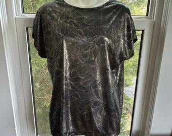 May include: A short-sleeved, black and gold metallic top with a swirling, abstract pattern. The top has a round neckline and is displayed on a mannequin. The fabric has a shiny, reflective quality.