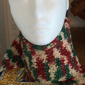 May include: A crocheted scarf with green, red, and beige stripes. The scarf is made with a sparkly yarn.