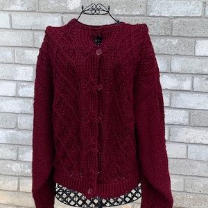 May include: A maroon knitted cardigan with a cable knit pattern and button closure.