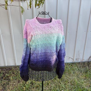 May include: A pastel ombre knitted sweater with a textured design and bobbles. The sweater is displayed on a black mannequin.