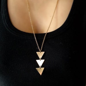 Puede incluir: Un collar de cadena dorada con un colgante hecho de tres triángulos dorados superpuestos.