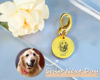 May include: A gold-toned circular pet tag featuring an engraved portrait of a dog and the name NALA, attached to a gold-toned lobster clasp. A pale yellow carnation flower is positioned next to the tag, alongside a circular photo of a golden dog.
