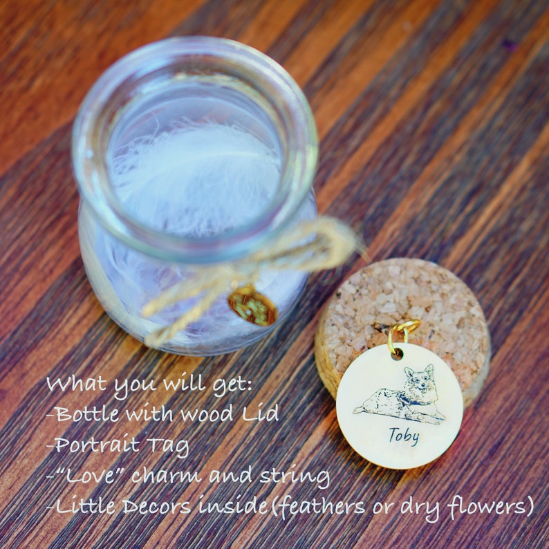 May include: A glass jar with a cork lid and a small metal tag with a pet portrait and the name "Toby". The jar contains a white feather and a small charm. The text "What you will get: -Bottle with wood Lid -Portrait Tag -"Love" charm and string -Little Decors inside (feathers or dry flowers)" is written below the jar.