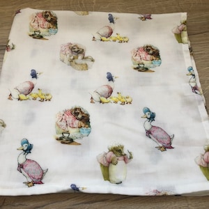 May include: White muslin baby swaddle with a repeating pattern of a duck and ducklings, a rabbit, and a hedgehog. The pattern is in shades of pink, blue, green, and yellow.