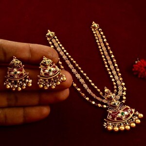 Peut inclure: Un collier en or avec trois rangs de cha&icirc;ne et un pendentif en &eacute;mail rouge, vert et blanc. Le pendentif est en forme de demi-lune et pr&eacute;sente un motif floral. Le collier est accompagn&eacute; de boucles d'oreilles assorties.