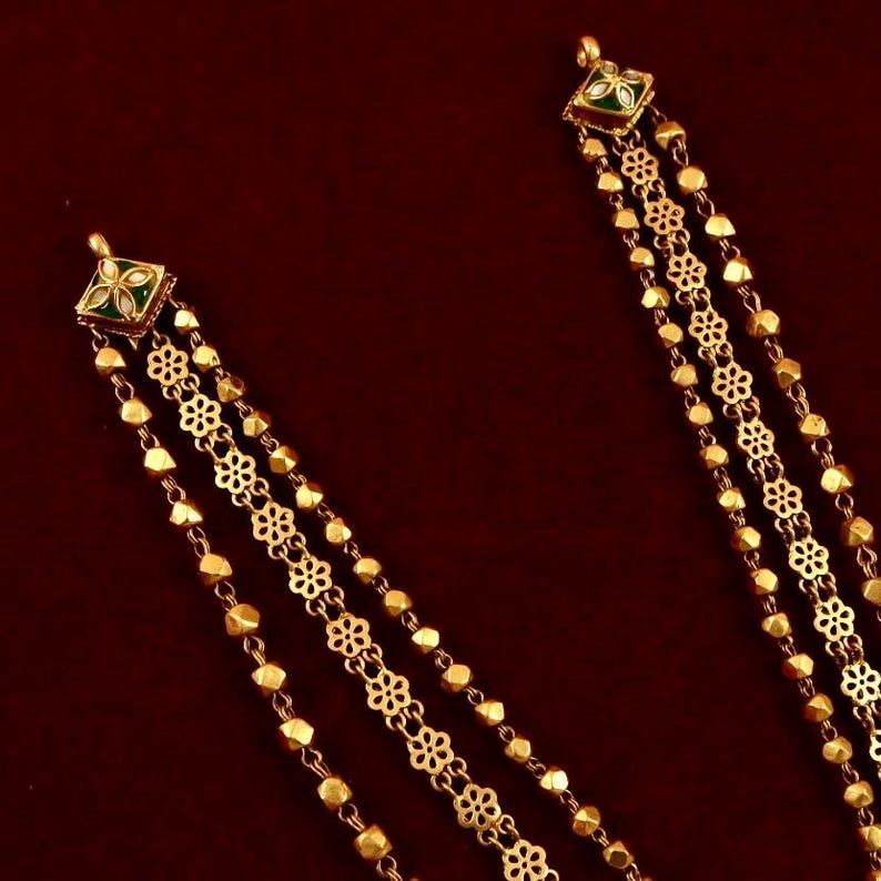 Peut inclure: Un collier en or compos&eacute; de trois rangs de cha&icirc;ne. Le rang central pr&eacute;sente un motif floral d&eacute;licat, tandis que les rangs ext&eacute;rieurs sont faits de perles rondes. Le collier a un pendentif carr&eacute; avec de l'&eacute;mail vert et blanc.