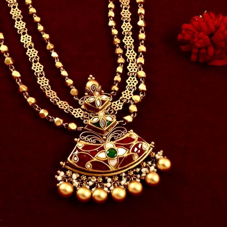 Peut inclure: Un collier en or avec une cha&icirc;ne &agrave; plusieurs rangs et un pendentif orn&eacute; d'un motif en &eacute;mail rouge, vert et blanc. Le pendentif est orn&eacute; de perles et a une base en forme d'&eacute;ventail.