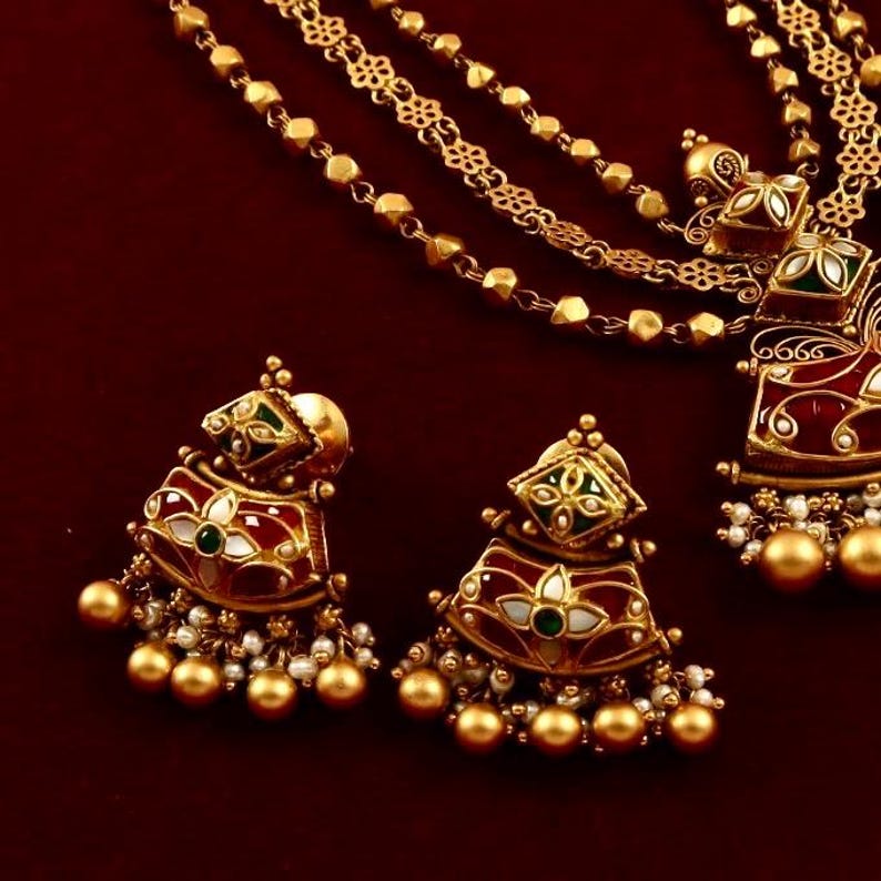 Peut inclure: Un collier en or avec une cha&icirc;ne &agrave; plusieurs rangs et un pendentif en &eacute;mail rouge, vert et blanc. Le pendentif est d&eacute;cor&eacute; de motifs floraux complexes. Des boucles d'oreilles assorties avec des &eacute;maux similaires et des accents de perles sont &eacute;galement incluses.