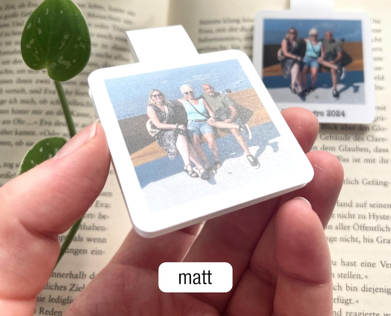 Ein personalisierbares magnetisches Lesezeichen mit Urlaubsfoto wird so in die Kamera gehalten, dass die matte Oberfläche gut zu erkennen ist. Darunter steht in einem weißen Feld der Text „matt".