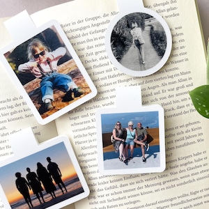 Auf einem aufgeklappten Buch liegen vier personalisierte Magnetlesezeichen in den Formaten rund, quadratisch, Quer- und Hochformat. Darauf zu erkennen sind persönliche Fotos von einzelnen Personen und Gruppen.